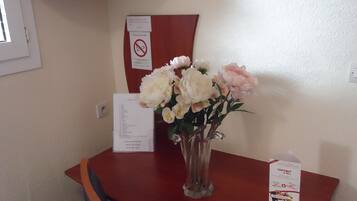 Habitación de hotel con una mesa de madera, un jarrón de flores, un televisor en un estante y un cartel de prohibido fumar en la pared.