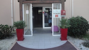 A hotel entrance with a wooden facade, glass doors, and a sign indicating a contact hotel. - L'Estuaire (Saint-Brevin-les-Pins)