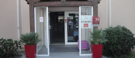 A hotel entrance with a wooden facade, glass doors, and a sign indicating a contact hotel.