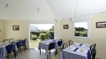 Un comedor con mesas dispuestas para cuatro, un ventanal con vistas a la vegetación y una puerta que da al exterior.