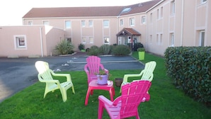 A building with a parking lot and a grassy area with four chairs and a small table. - L'Estuaire (Saint-Brevin-les-Pins)