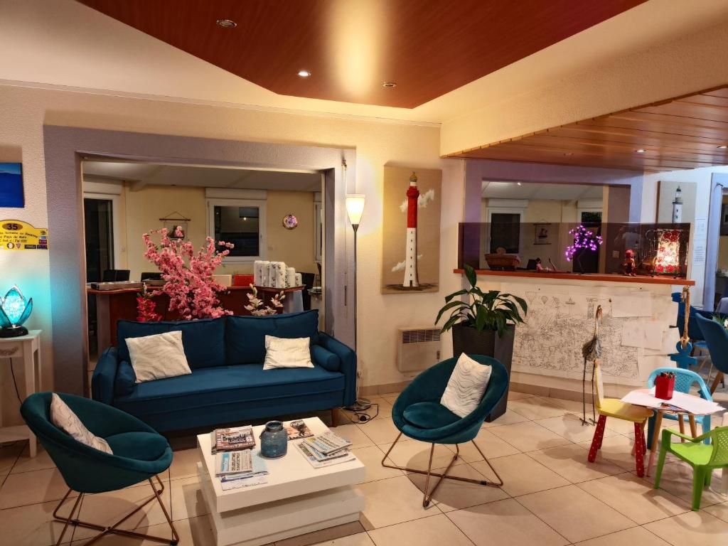 Ein Wohnzimmer mit einem blauen Sofa, zwei türkisfarbenen Sesseln, einem Couchtisch und einer Küchenzeile im Hintergrund.