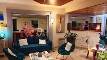 Ein Wohnzimmer mit einem blauen Sofa, zwei türkisfarbenen Sesseln, einem Couchtisch und einer Küchenzeile im Hintergrund.