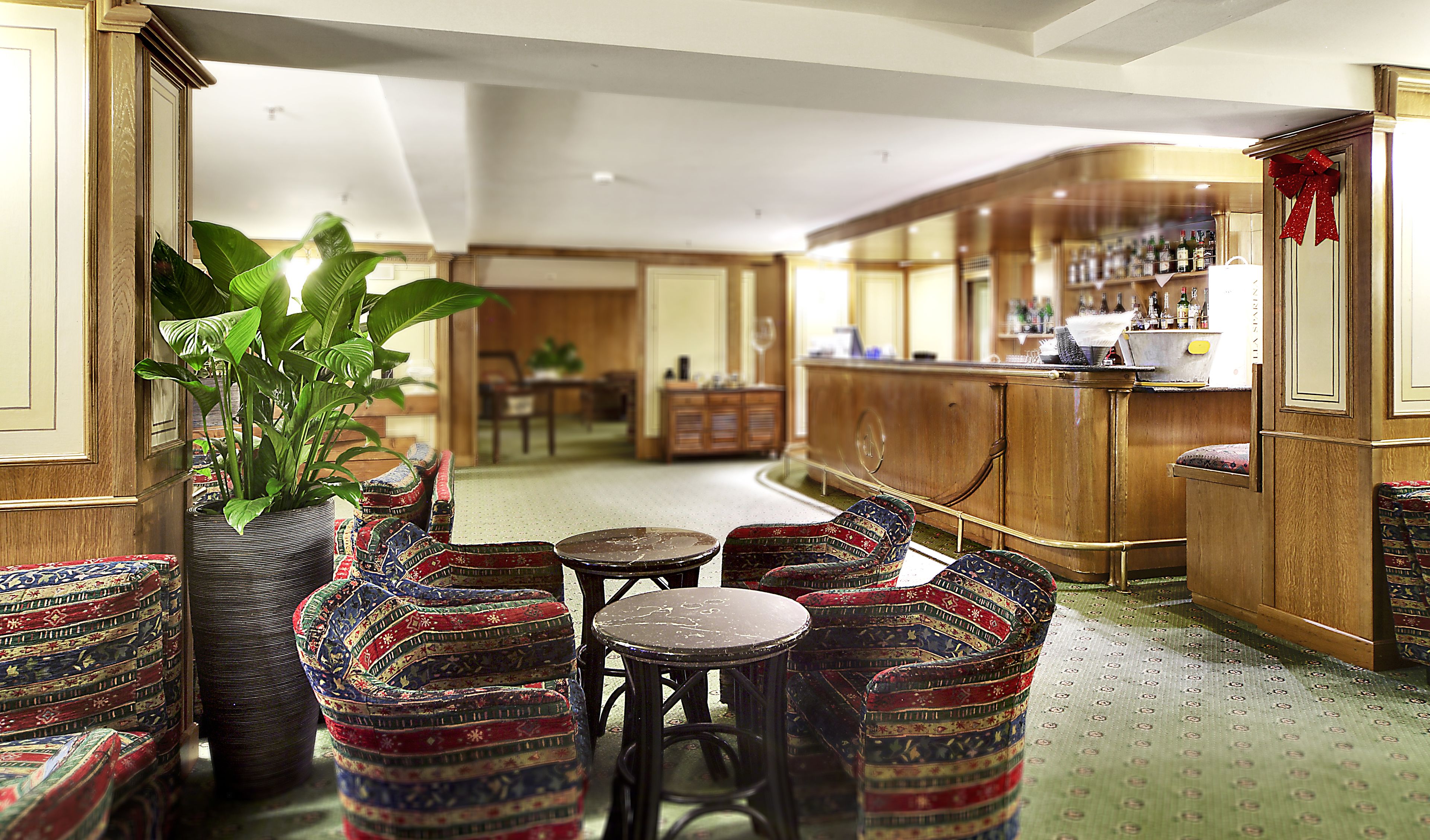 A bar area with patterned chairs, a large potted plant, and a bar counter with bottles.