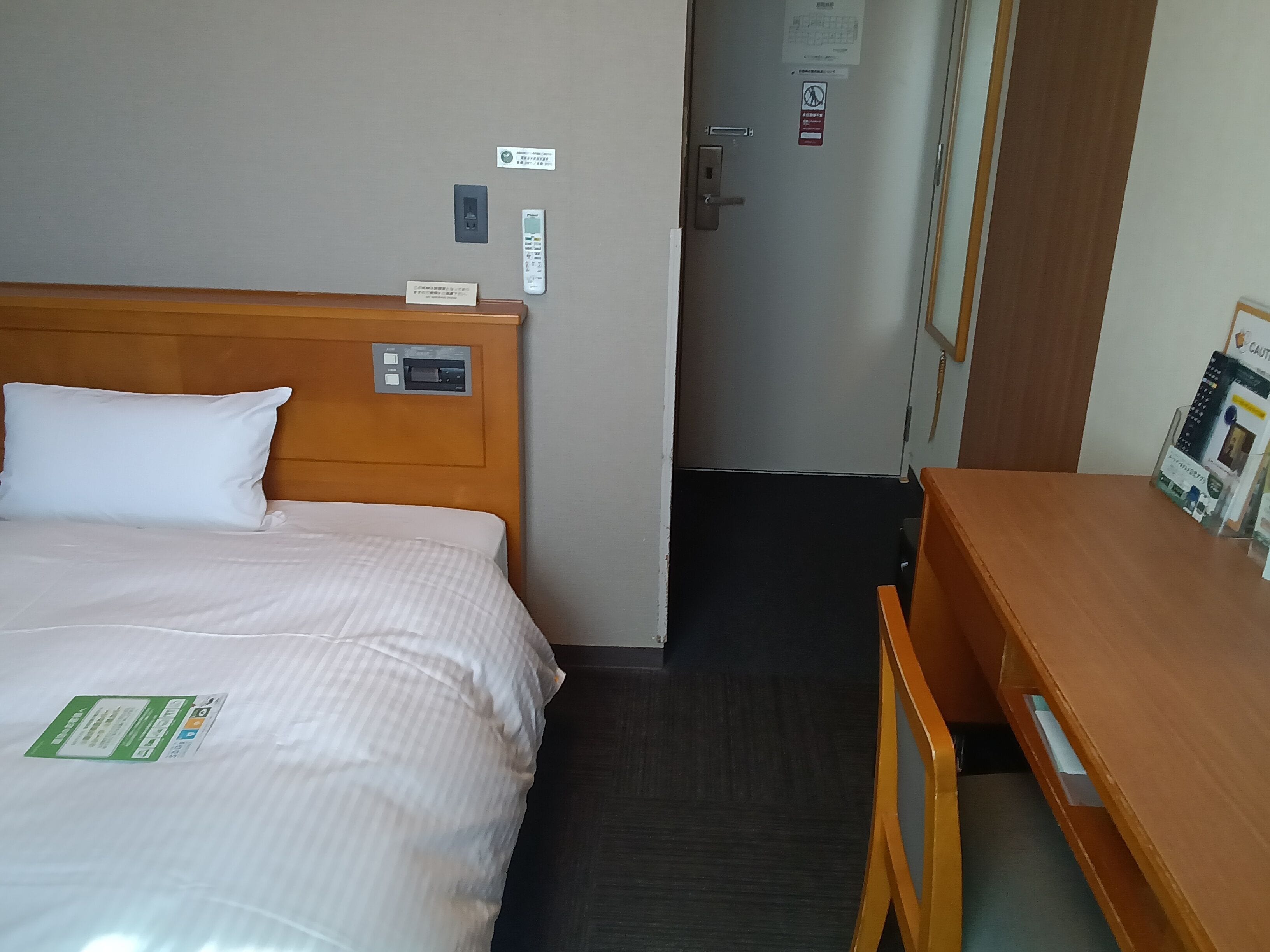 Een hotelkamer met een bed, nachtkastje, bureau en een deur die uitkomt in een gang.