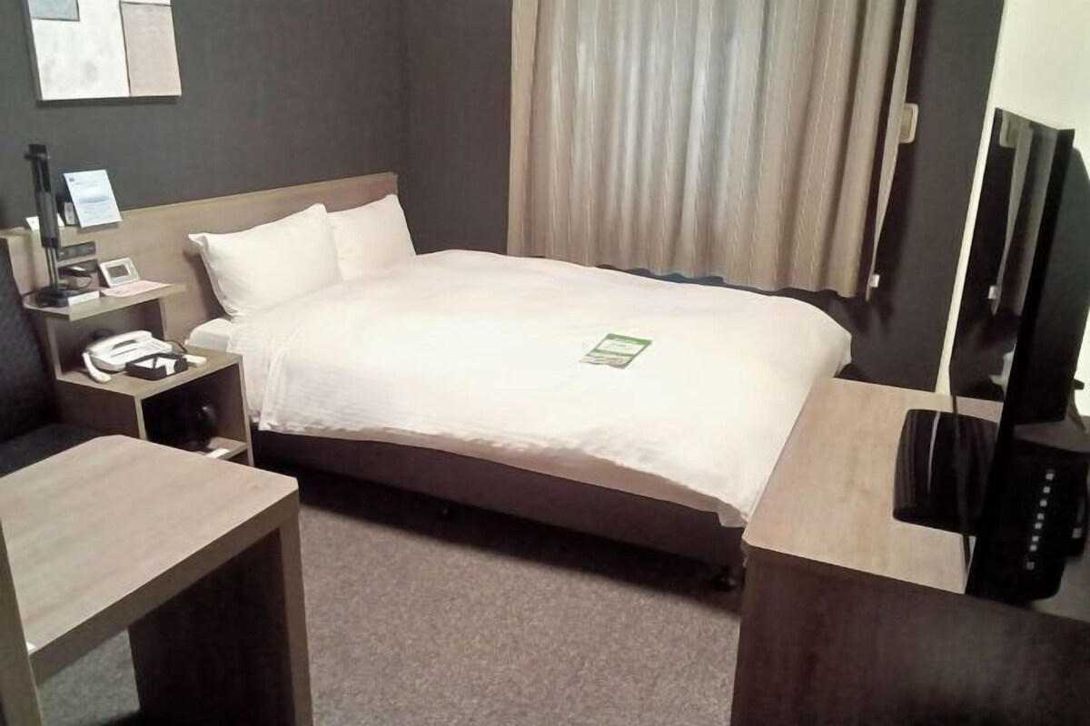 A hotel room with a bed, bedside table, lamp, phone, and a TV.