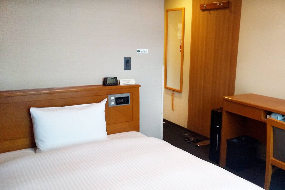 Una camera d'albergo con un letto, un comodino, una scrivania e uno specchio.
