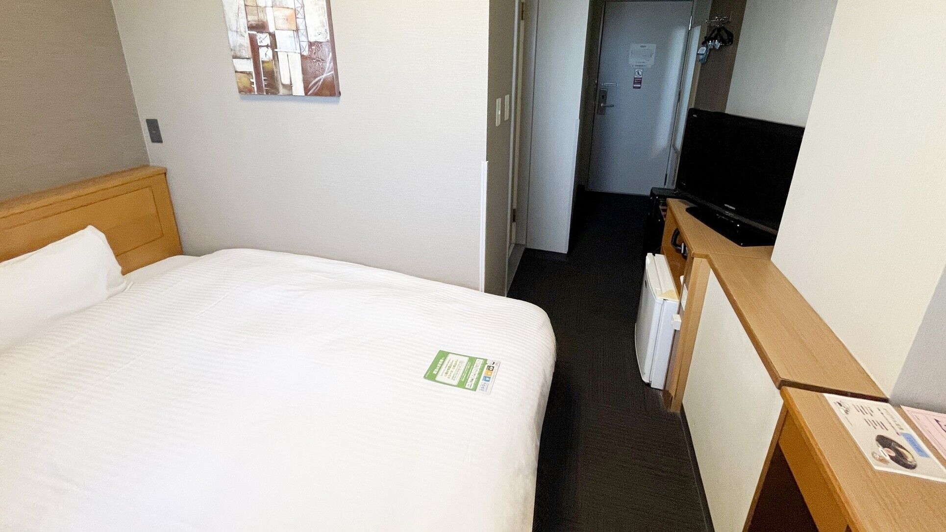 A hotel room with a bed, a television, a desk, and a door leading to a hallway.