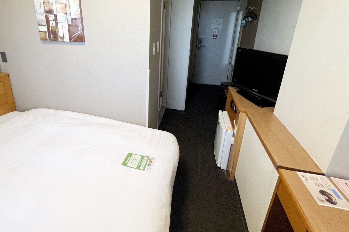 A hotel room with a bed, a television, a desk, and a door leading to a hallway.