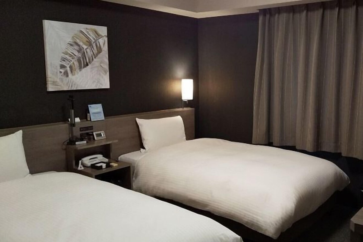 A hotel room with two beds, a nightstand with a phone, a lamp, and a painting on the wall.