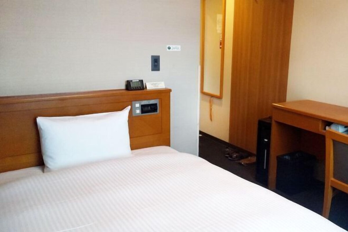 A hotel room with a bed, a bedside table, a telephone, and a mirror.