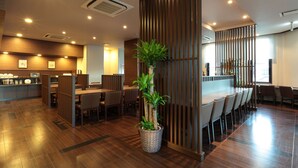 A modern restaurant with wooden flooring, a central dining area with high tables and chairs, and a counter with a display of items. - Hotel Route - Inn Toyota Jinnaka (Toyota)