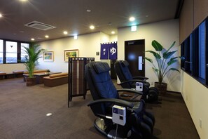 A massage therapy room with two massage chairs, a reception desk, a bench, and a large window with a view.