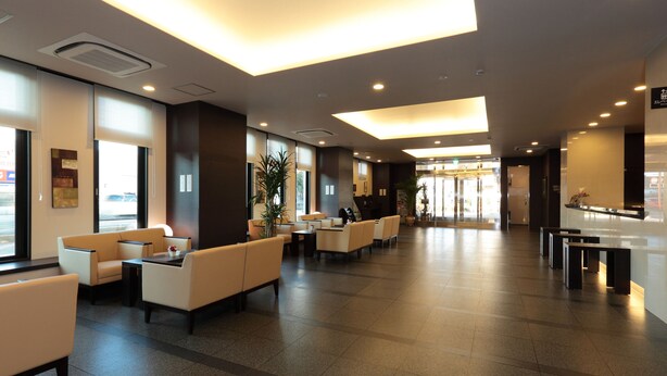 A spacious lobby with seating areas, a reception desk, and large windows allowing natural light. - Hotel Route - Inn Toyota Jinnaka (Toyota)