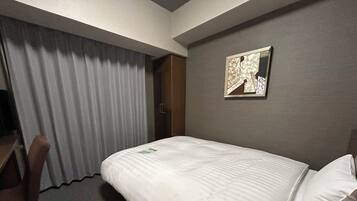 A hotel room with a bed, a chair, a desk, and a painting on the wall.