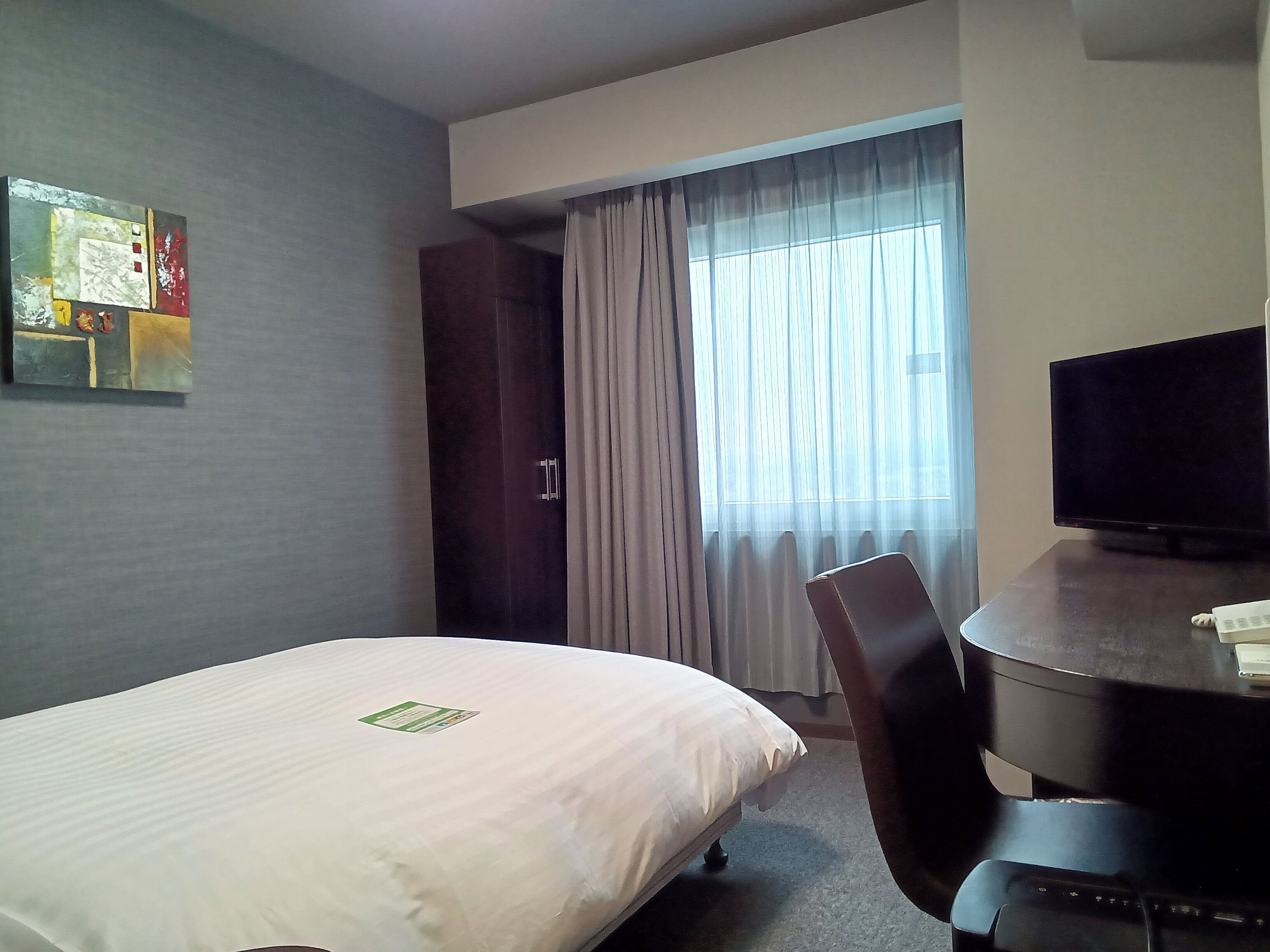 A hotel room with a bed, a desk with a computer, a television, and a window with curtains.