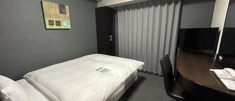 Una habitación de hotel con una cama individual, un escritorio con silla, televisión y ventana con cortinas.