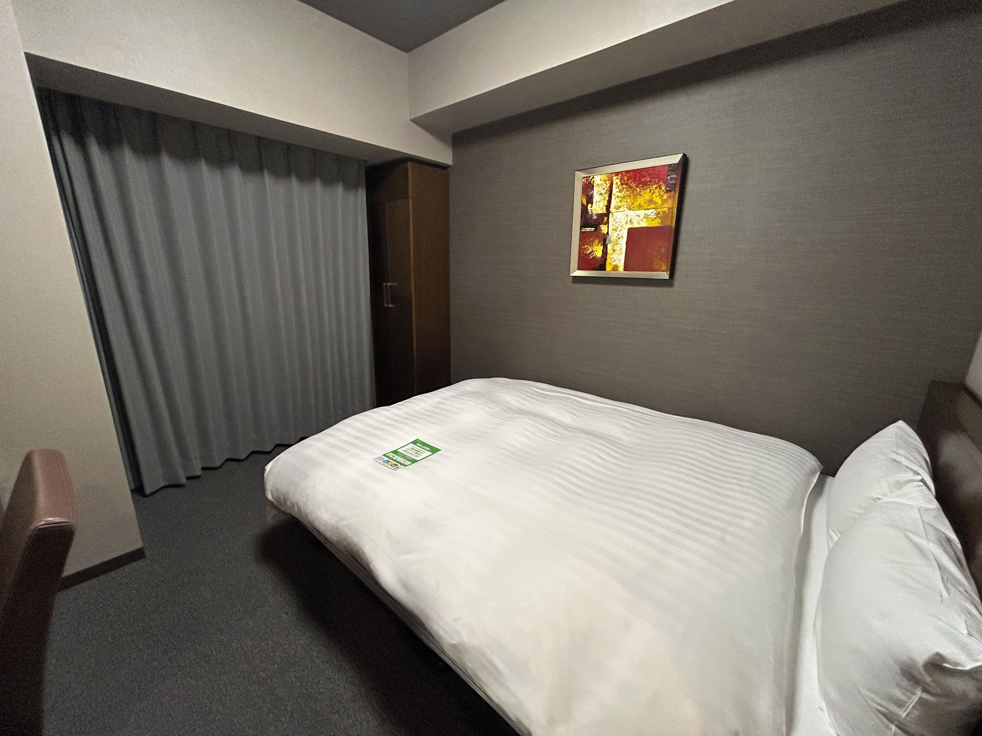 Une chambre d’hôtel avec un lit, un tableau au mur et un rideau.