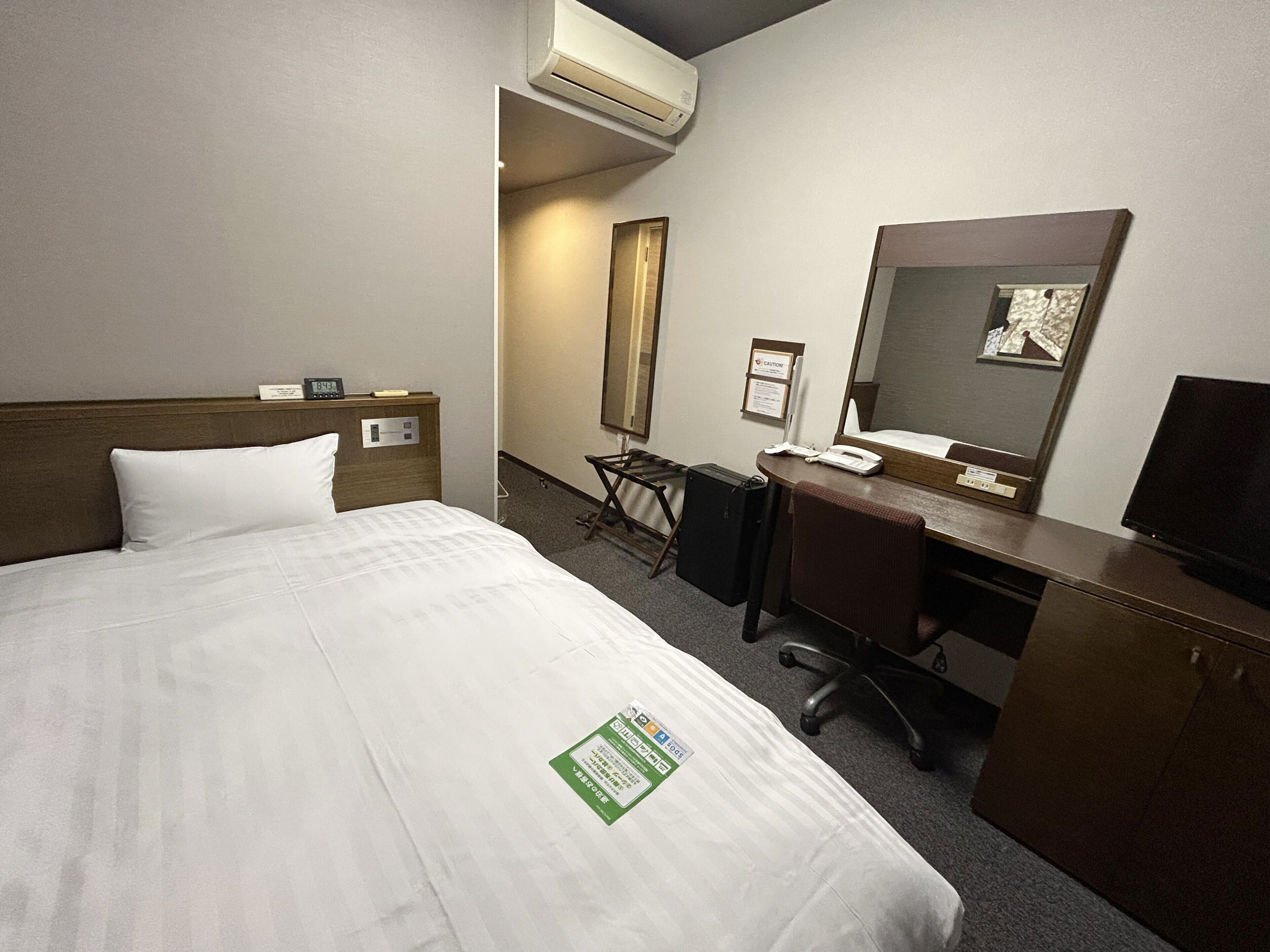 Een hotelkamer met een bed, een bureau, een stoel, een bureaulamp, een telefoon en een televisie.