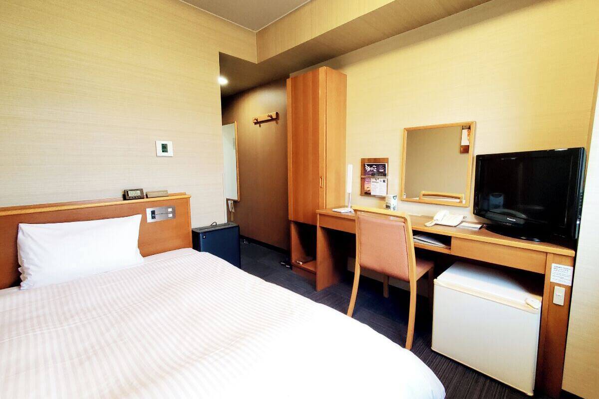 Een hotelkamer met een bed, een bureau, een televisie en een kleine koelkast.