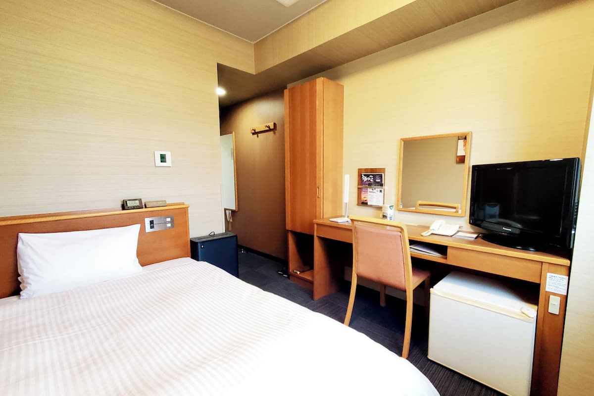 Een hotelkamer met een bed, bureau, stoel, televisie en een kleine koelkast.