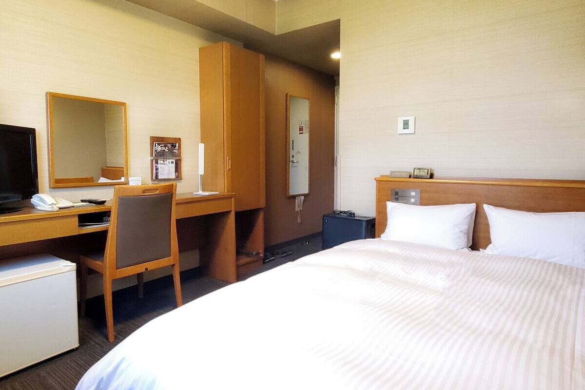 Een hotelkamer met een bed, een bureau met stoel, een televisie, een koelkast en een spiegel.