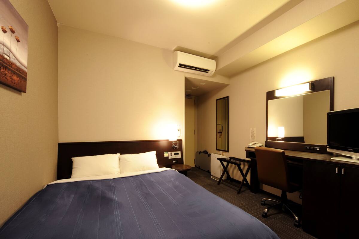 A hotel room with a bed, desk, chair, and a large mirror.