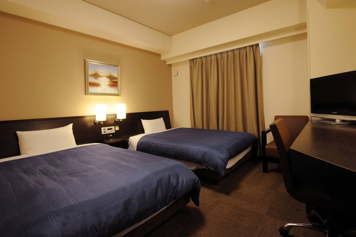 A hotel room with two beds, a desk, a TV, and a painting on the wall.