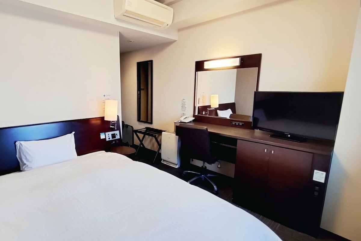 Une chambre d’hôtel avec un lit, un bureau avec une télévision, un miroir et une lampe.