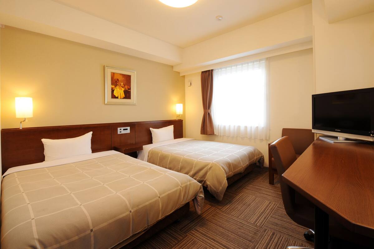 A hotel room with two beds, a desk, a television, and a painting on the wall.