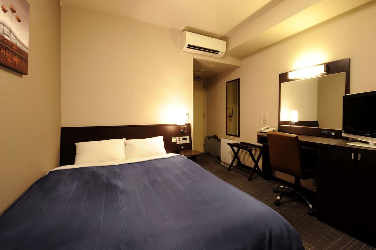 A hotel room with a bed, desk, chair, and a large mirror.