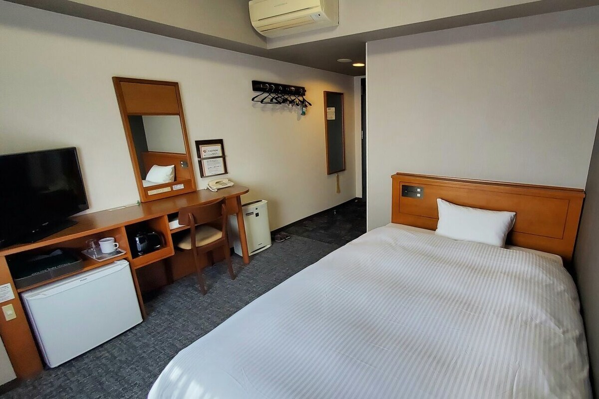 A hotel room with a bed, a desk with a computer, a television, and a mini-fridge.