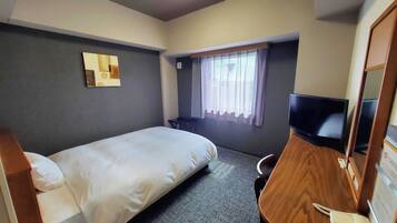 Habitación de hotel con cama, escritorio con teléfono, televisión, ventana con cortinas y lámpara de pared.