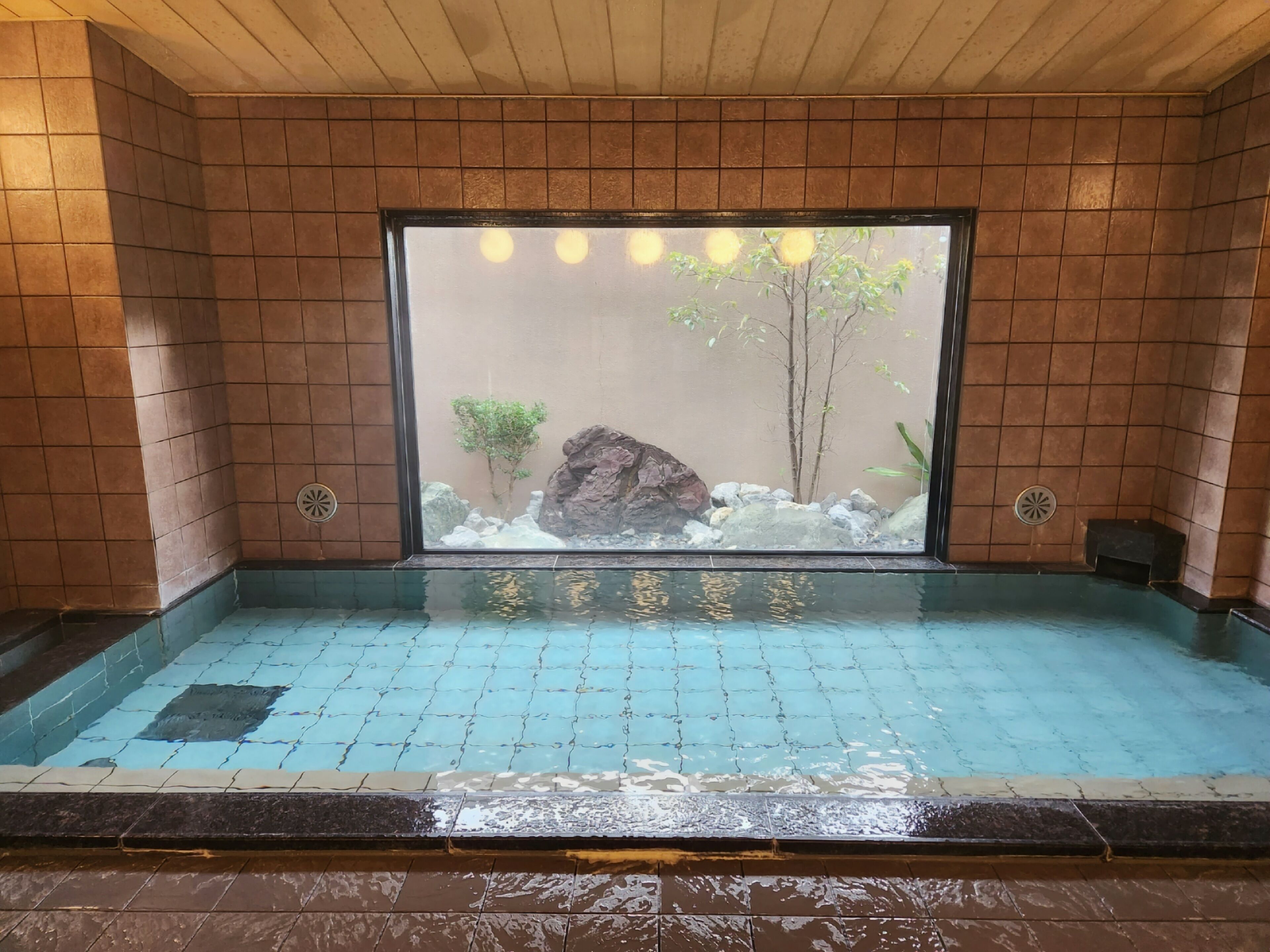 Una piscina interior pequeña con vistas a un jardín de rocas a través de una pared de cristal.