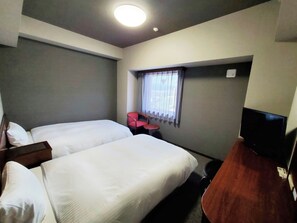 A hotel room with two beds, a small table, a chair, a television, and a window with curtains.