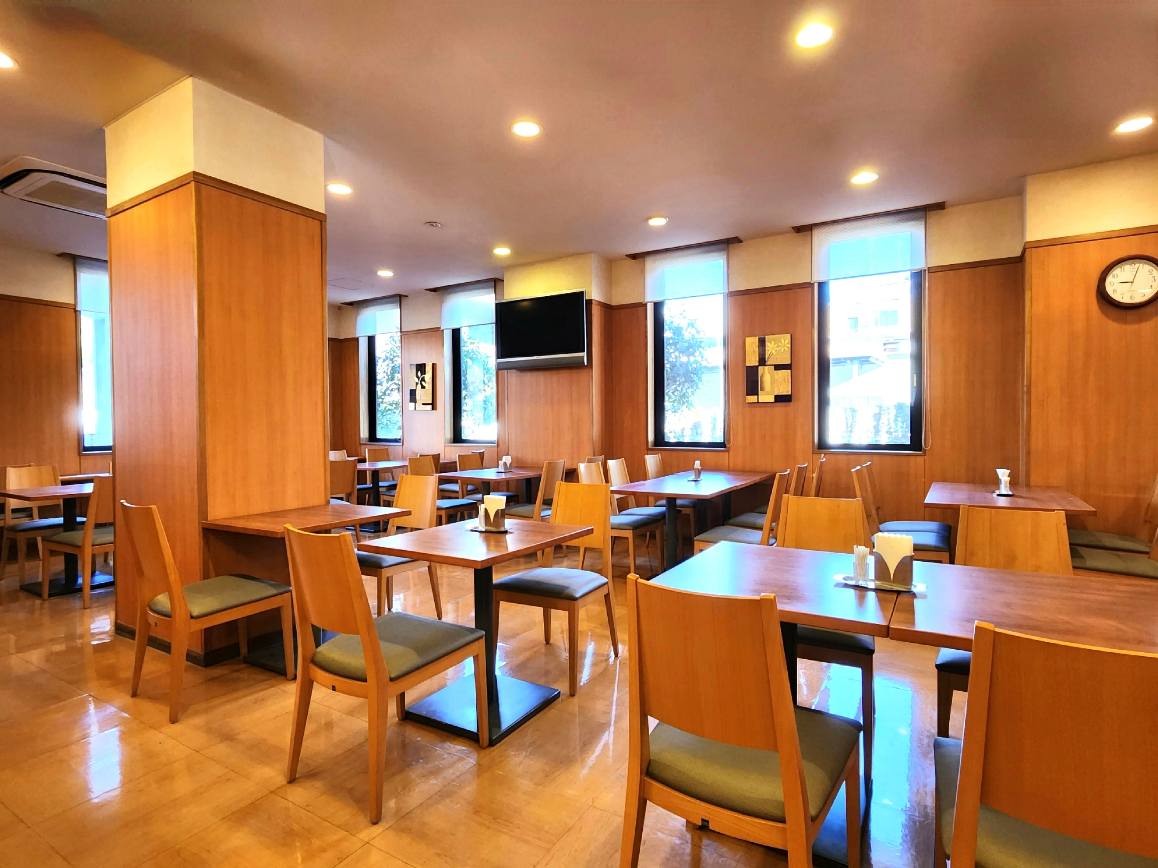 Un restaurant avec des tables et des chaises en bois, de grandes fenêtres et une horloge au mur.