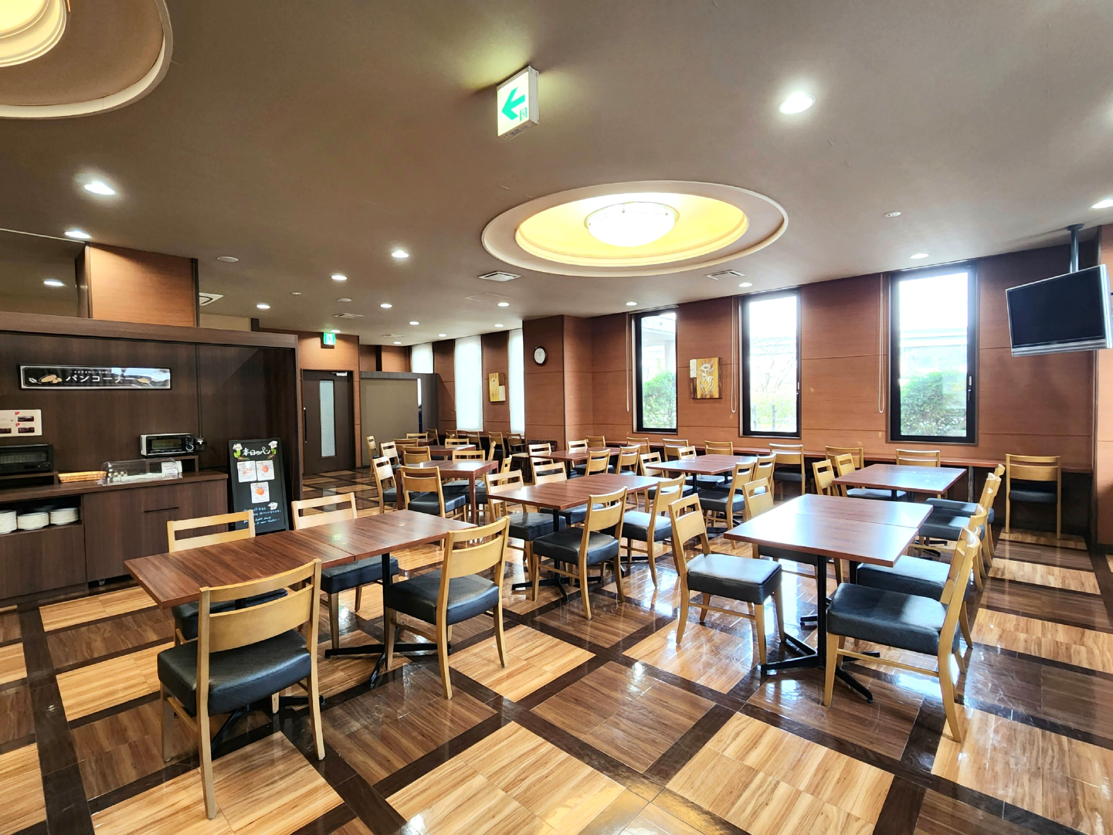 A restaurant with multiple tables and chairs, a kitchen area, and large windows.
