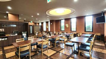 A restaurant with multiple tables and chairs, a kitchen area, and large windows.
