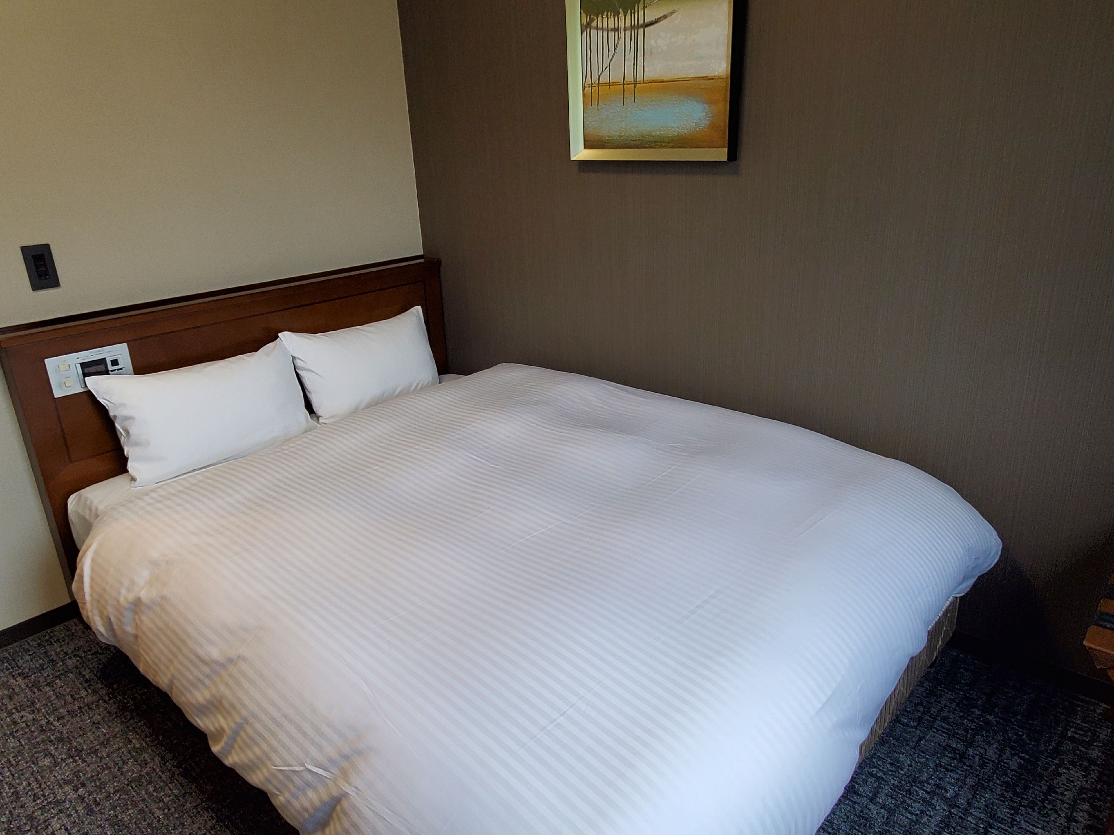 A hotel room with a large bed, a headboard with a control panel, and a painting on the wall.