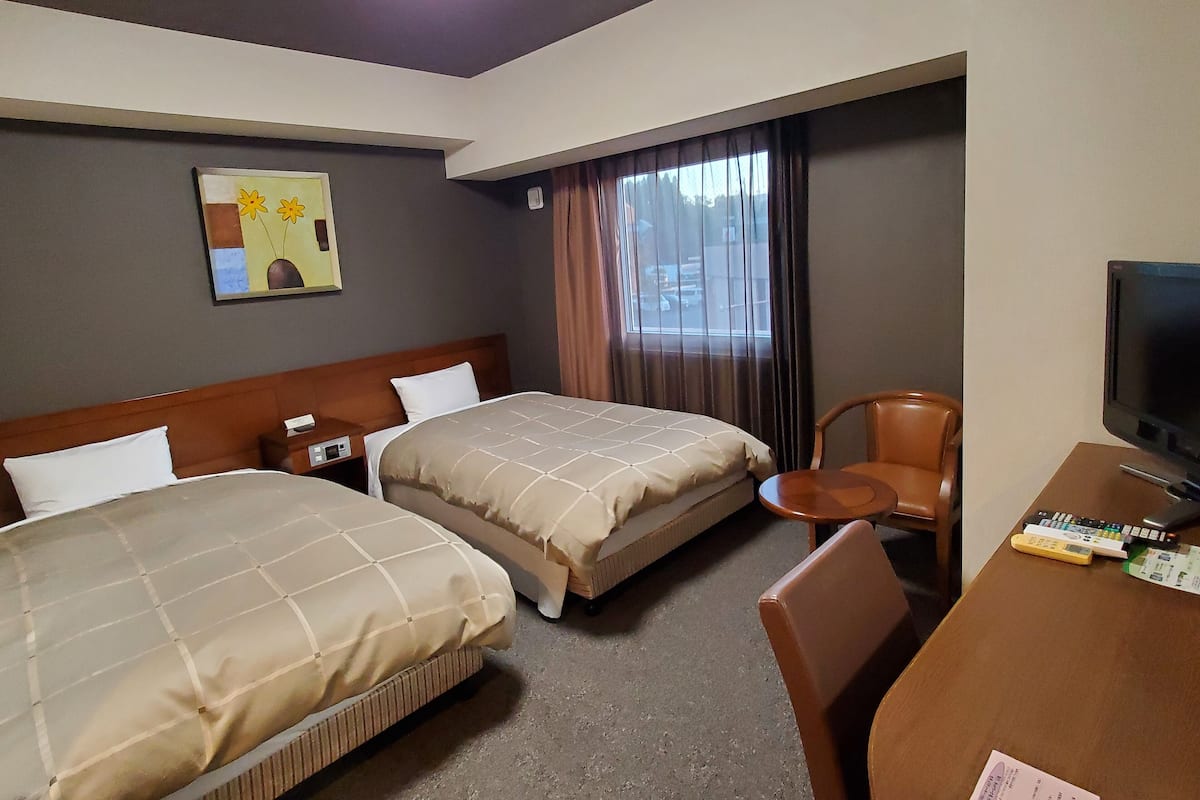 Een hotelkamer met twee bedden, een bureau met een televisie en een stoel.