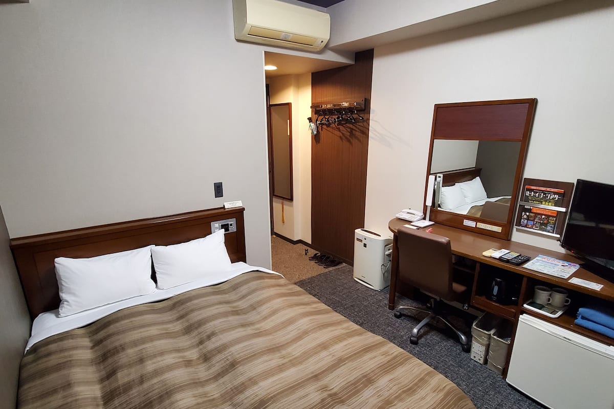Een hotelkamer met een bed, bureau, stoel, televisie en koelkast.