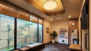 A hotel lobby with a seating area, a vending machine, a clock, and a view of the outside.