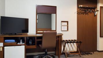 Une chambre d’hôtel équipée d’un bureau, d’une télévision, d’un mini-réfrigérateur, d’une chaise, d’un porte-manteau et d’une porte.