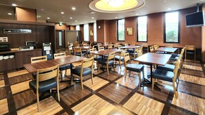 A restaurant with multiple tables and chairs, a kitchen area, and large windows.