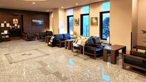 A hotel lobby with a reception desk, seating area, framed artwork, and large windows.