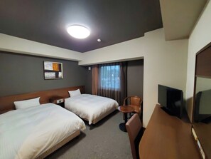 Een hotelkamer met twee bedden, een bureau met stoel, een televisie en een raam met gordijnen.