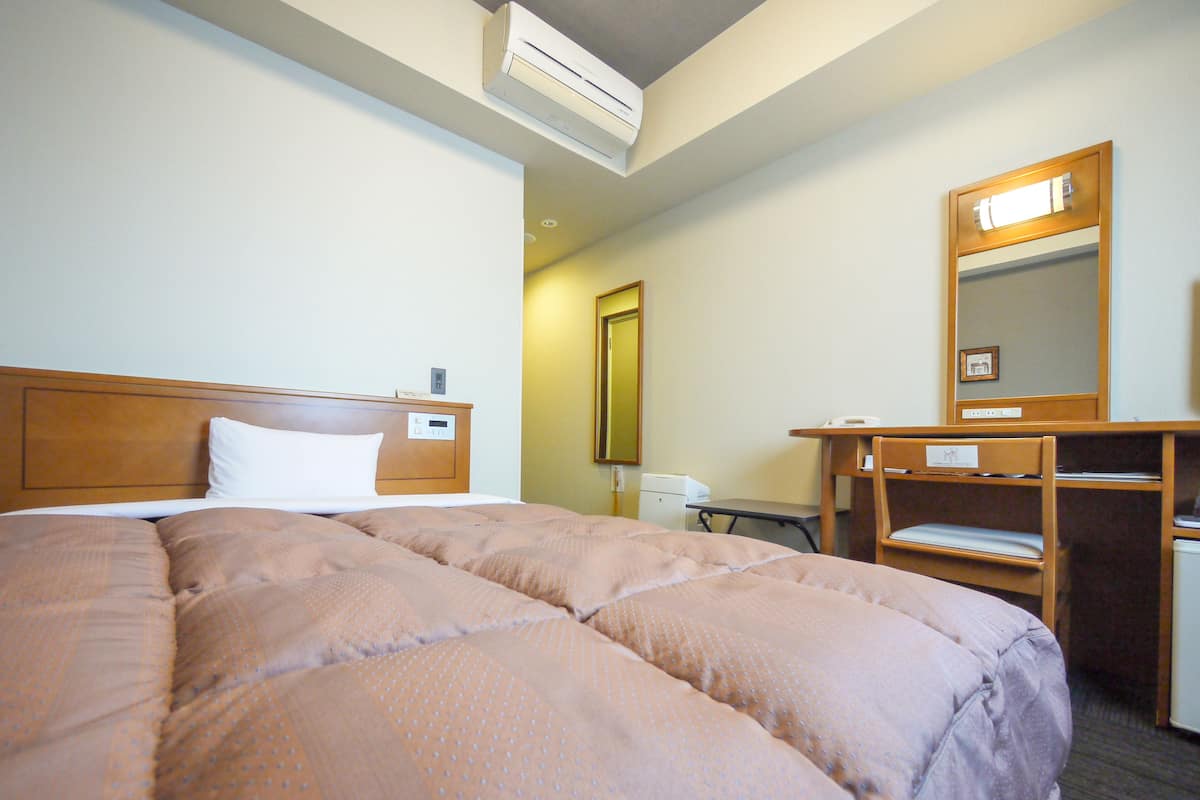 Una habitación de hotel con una cama grande, un escritorio, una silla, un espejo y un equipo de aire acondicionado.