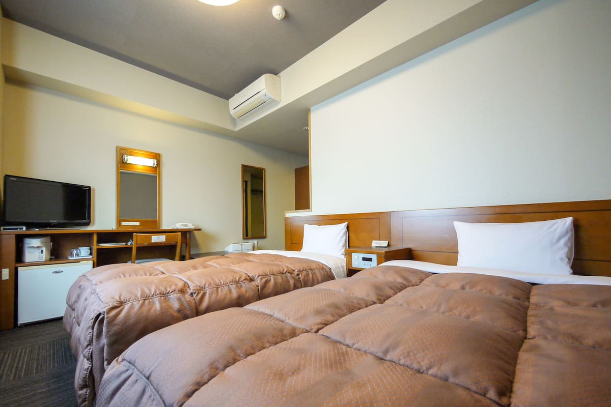 Una habitación de hotel con dos camas, televisión, escritorio y cafetera.
