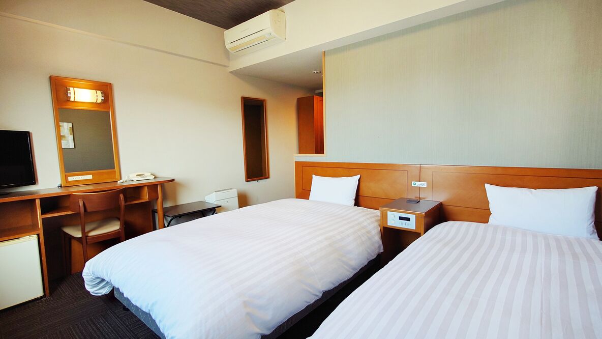 Ein Hotelzimmer mit zwei Betten, einem Schreibtisch mit Stuhl, einem Fernseher und einem Spiegel.