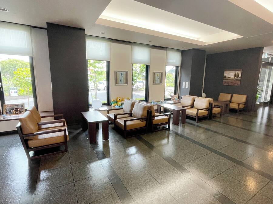 Un vestíbulo amplio con diseño moderno, que incluye una zona de estar con sofás y sillones, un mostrador de recepción y grandes ventanales que dejan entrar luz natural.